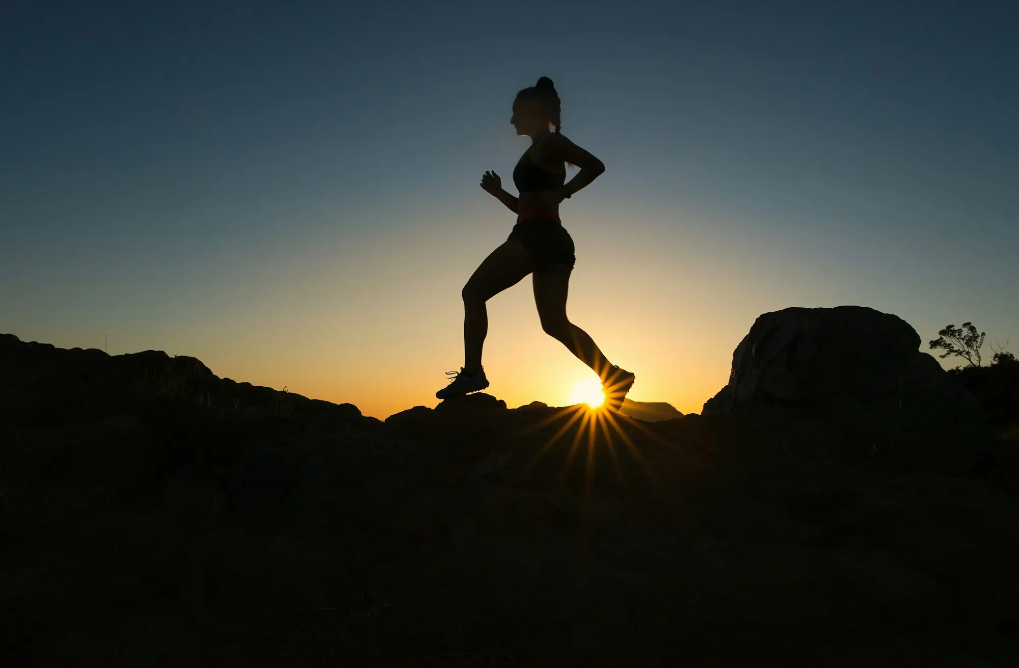 A runner against a low sun on a rocky trail